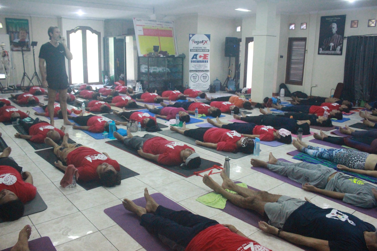 How Many Men Do Yoga? The Rise of Men in the Hot Room Report 3 Rows of students lying in Savasana across a large hall while the instructor stands at the front of the room