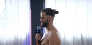 A bearded male trainee holding a microphone while practising his dialogue delivery in front of the class