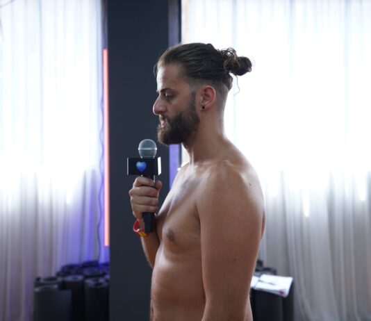 A bearded male trainee holding a microphone while practising his dialogue delivery in front of the class
