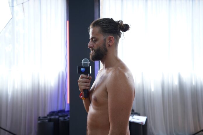 how-many-men-do-yoga-male-trainee-practical-teaching A bearded male trainee holding a microphone while practising his dialogue delivery in front of the class
