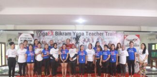 A YogaFX teacher training intake photographed together on stage beneath the Bikram Hot 26 and 2 banner in Bali